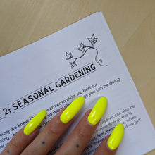 Load image into Gallery viewer, Black text on white paper reads &quot;Seasonal Gardening&quot; with a flourish of ivy in the top right corner.  Boss Witch&#39;s hand is on the page too &amp; their nails are fluorescent green. 