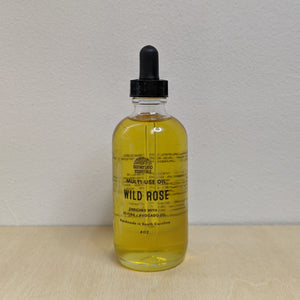 Glass bottle with black dropper lid containing golden multi use oil by Motherland Essentials reads "wild rose" in black block letters available at Coyote Supply Co, a zero waste witch store in Midtown Reno, Nevada that is BIPOC owned