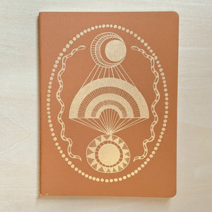 Open dated 6 month planner cover featuring a gold moon, rainbow, and sun framed by two snakes and dots on orange paper.  Made by The Rainbow Vision, sold at zero waste witch store Coyote Supply Co in Midtown Reno, Nevada