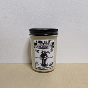 White soy wax candle in glass jar with black lid.  Features a white label with black inked artwork of Mama Muerte by Firme Arte available at Coyote Supply Co, a zero waste witch store in Midtown Reno, Nevada that is BIPOC owned