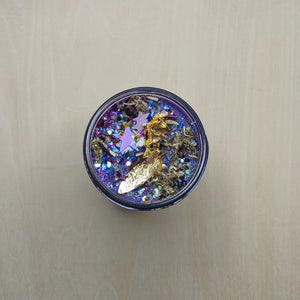 Purple soy wax candle topped with gold leaf, glitter, star confetti, and mugwort available at Coyote Supply Co, a zero waste witch store in Midtown Reno, Nevada that is BIPOC owned