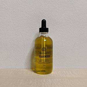 Glass bottle with black dropper lid containing golden multi use oil by Motherland Essentials reads "teakwood" in black block letters available at Coyote Supply Co, a zero waste witch store in Midtown Reno, Nevada that is BIPOC owned