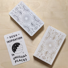 Load image into Gallery viewer, (clockwise from bottom left corner) white oracle card with black drawing of a starry staircase portal reads &quot;seek inspiration in unusual places&quot;, stacked card deck features gilded edges &amp; magical symbol motifs in black, deck box featuring magical symbol motifs in gold by Worthwhile Paper available at Coyote Supply Co, a zero waste witch store in Midtown Reno, Nevada that is BIPOC owned