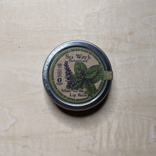 Load image into Gallery viewer, Round metal tin with round kraft paper label featuring a green boarder &amp; a sprig of mint containing vegan lip balm by Sea Witch Botanicals available at Coyote Supply Co, a zero waste witch store in Midtown Reno, Nevada that is BIPOC owned