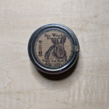 Load image into Gallery viewer, Round metal tin with round kraft paper label featuring a blue boarder &amp; a fluffy bunny containing vegan lip balm by Sea Witch Botanicals available at Coyote Supply Co, a zero waste witch store in Midtown Reno, Nevada that is BIPOC owned