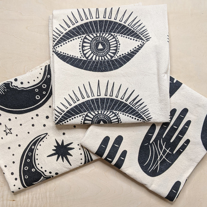 3 zero waste universal cloths.  Black ink on unbleached cotton, left to right: crescent moons, eyes, hands.  Witch made by The Rainbow Vision available at Coyote Supply Co, a zero waste witch store in Midtown Reno, Nevada that is BIPOC owned