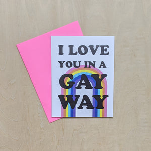 Hot pink envelope & white card featuring a central rainbow & black text that reads "I love you in a gay way."  Card by Ash & Chess, sold by zero waste witch store Coyote Supply Co in Reno, Nevada.