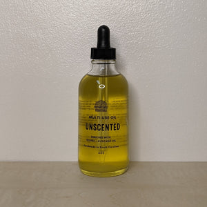 Glass bottle with black dropper lid containing golden multi use oil by Motherland Essentials reads "unscented" in black block letters available at Coyote Supply Co, a zero waste witch store in Midtown Reno, Nevada that is BIPOC owned