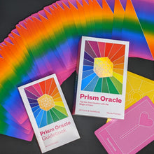 Load image into Gallery viewer, Prism Oracle Deck by Nicole Pivirotto. Image shows a fan of rainbow cards across the image. Resting on top of this is a white guidebook with artwork featuring a rainbow bursting out of a holographic gold prism. Box featuring the same art work sits next to it. In the lower left corner, a pink card reads &quot;sweetness&quot; and features an image of a heart shaped lollipop. Available at Coyote Supply Co, a zero waste witch store in Midtown Reno, Nevada that is BIPOC owned