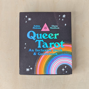 Black box of tarot cards by Ash + Chess features a black image of a rainbow in the colors of the POC inclusive pride flag and the trans pride flag. Box reads "Queer Tarot an Inclusive Deck & Guidebook" in blue holographic lettering available at Coyote Supply Co, a zero waste witch store in Midtown Reno, Nevada that is BIPOC owned