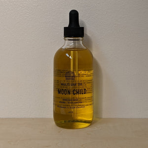 Glass bottle with black dropper lid containing golden multi use oil by Motherland Essentials reads "moon child" in black block letters available at Coyote Supply Co, a zero waste witch store in Midtown Reno, Nevada that is BIPOC owned