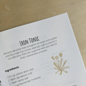 Inner page detail of “Simple Home Herbal Recipes” by Safiyyah Bazemore of Nour Herbals.  White paper page features a recipe for an iron tonic in black text with a mustard yellow illustration of a dandelion.  Available at Coyote Supply Co a zero waste witch store located in Midtown Reno, Nevada that is BIPOC owned.