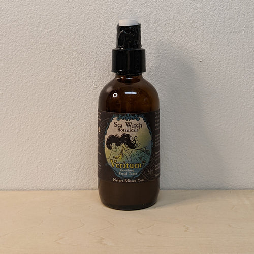 An amber glass bottle with a black label that has a blue/yellow colored frame in the center. The label reads 
Sea Witch Botanicals
Veritum 
Soothing Facial Toner
Nature Misses You