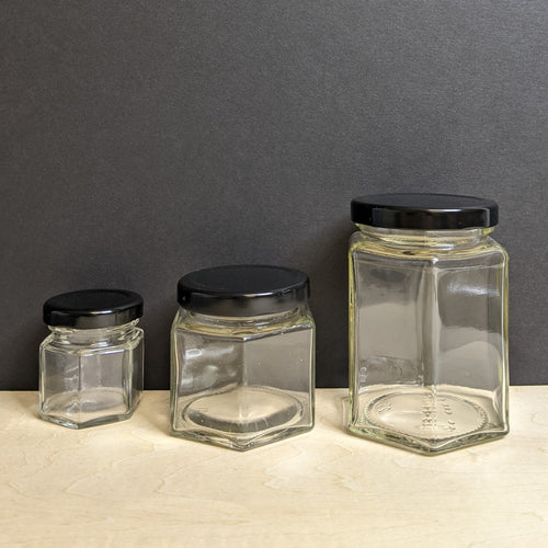 Three clear hexagon shaped glass jars with black metal lids. They are arranged in smallest to largest. Sold at Coyote Supply Co a BIPOC and LGBTQIA+ owned zero waste witch store in Reno Nevada