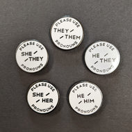 Five round white enamel pins with black text on a black background. Going clockwise the pins read:
PLEASE USE THEY/THEM PRONOUNS
PLEASE USE HE/THEY PRONOUNS
PLEASE USE HE/HIM PRONOUNS
PLEASE USE SHE/HER PRONOUNS
PLEASE USE SHE/THEY PRONOUNS 

Sold at Coyote Supply Co a BIPOC and LGBTQIA+ owned zero waste witch store in Reno Nevada