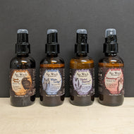 Four amber glass bottles on a black background. The bottles each has a black label with a colored frame in the center that says Sea Witch Botanicals Scented Veil. From left to right the labels are 
orange with an illustration of a raven Quoth the Raven, blue with an illustration of a great horned owl White Lodge, purple with an illustration of a bee on lavender Herbal Renewal, red with an illustration of a fox Hermitage.
Sold at Coyote Supply Co a BIPOC and LGBTQIA+ owned zero waste witch store in Reno NV