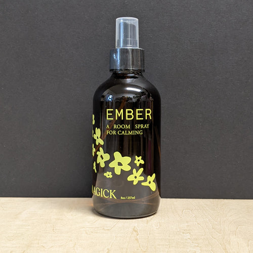 An 8oz dark amber glass bottle with a spray top that reads: Ember A Room Spray For Calming. Sold at Coyote Supply Co a BIPOC and LGBTQIA+ owned zero waste witch store in Reno Nevada