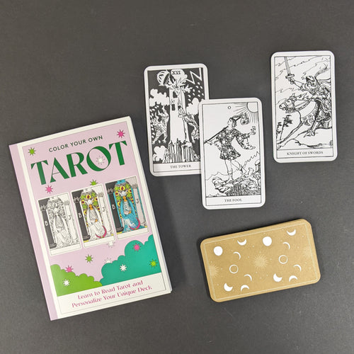 A light purple box that reads Color Your Own Tarot in green text, the box also features images of the High Priestess card in black and white and various states of color. Next to the box are uncolored black and white versions of The Tower, The Fool, and the Knight of Swords. Below the cards is the back of a card, it is light brown with white stars, moons, and suns. All on a black background.  Sold at Coyote Supply Co a BIPOC and LGBTQIA+ owned zero waste witch store in Reno Nevada